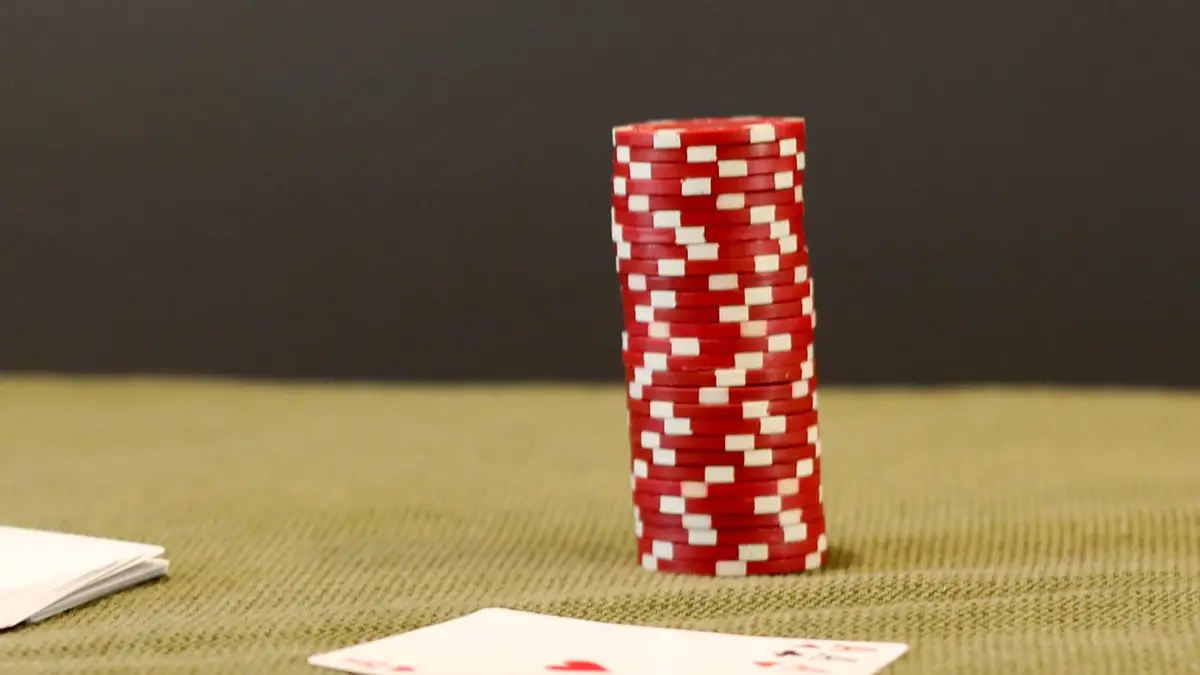 A tall stack of red poker chips standing on green felt beside face-down cards