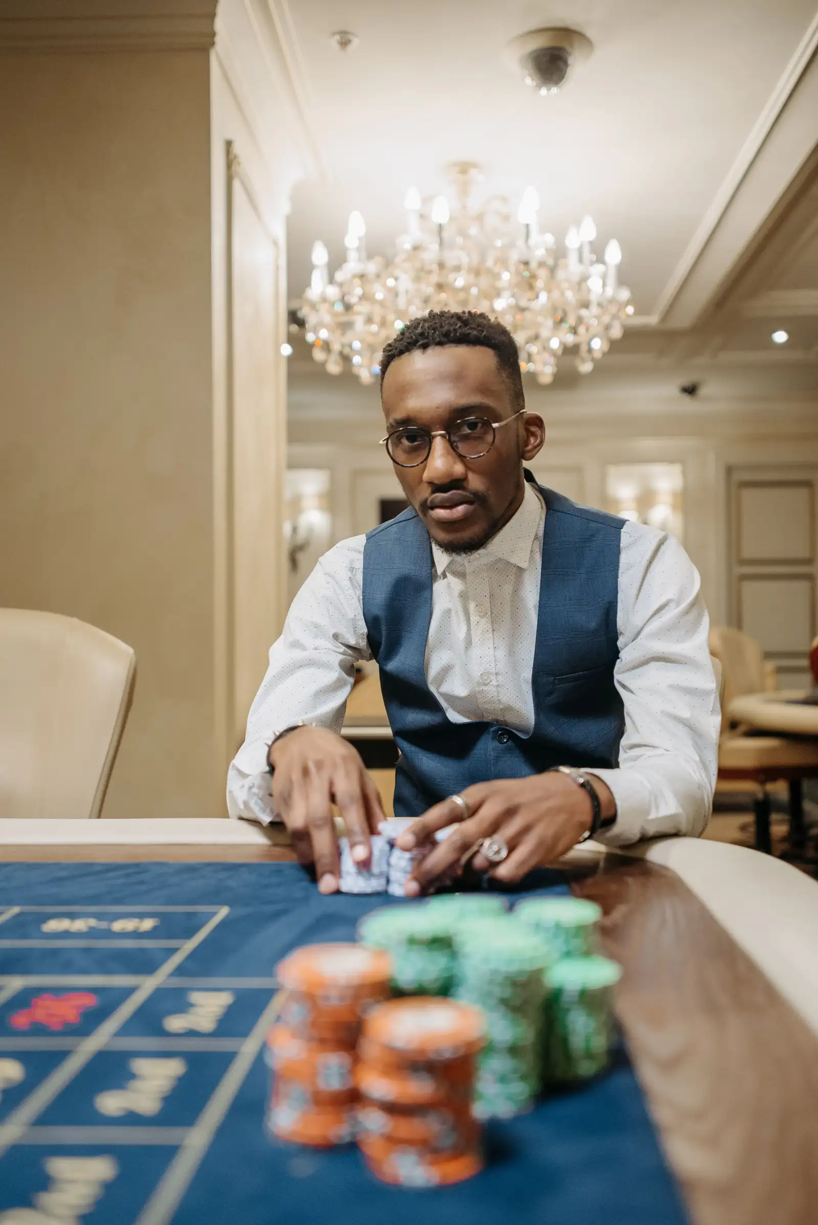 A player reaching for chips at a casino roulette table beneath a grand chandelier