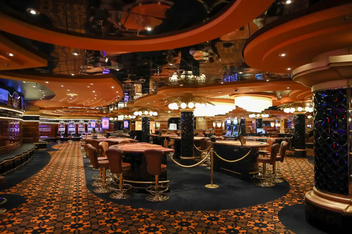 A lavish casino floor with chandeliers, gold trim and card tables under warm light
